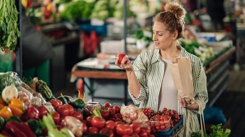 Portrait of female customer standing near market stall with paper bag in hands and shopping fresh organic tomato at farmer's market. Young shopper woman purchasing fresh products at food market.; Shutterstock ID 2455755411