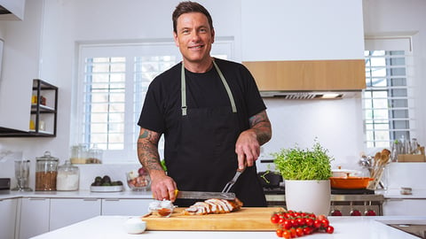 Chef Chuck Hughes standing at a kitchen counter cutting slices of turkey