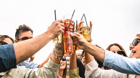 Group of young friends raises plastic glasses with spritz and fruit cocktails for a celebrate toast against a white background sky