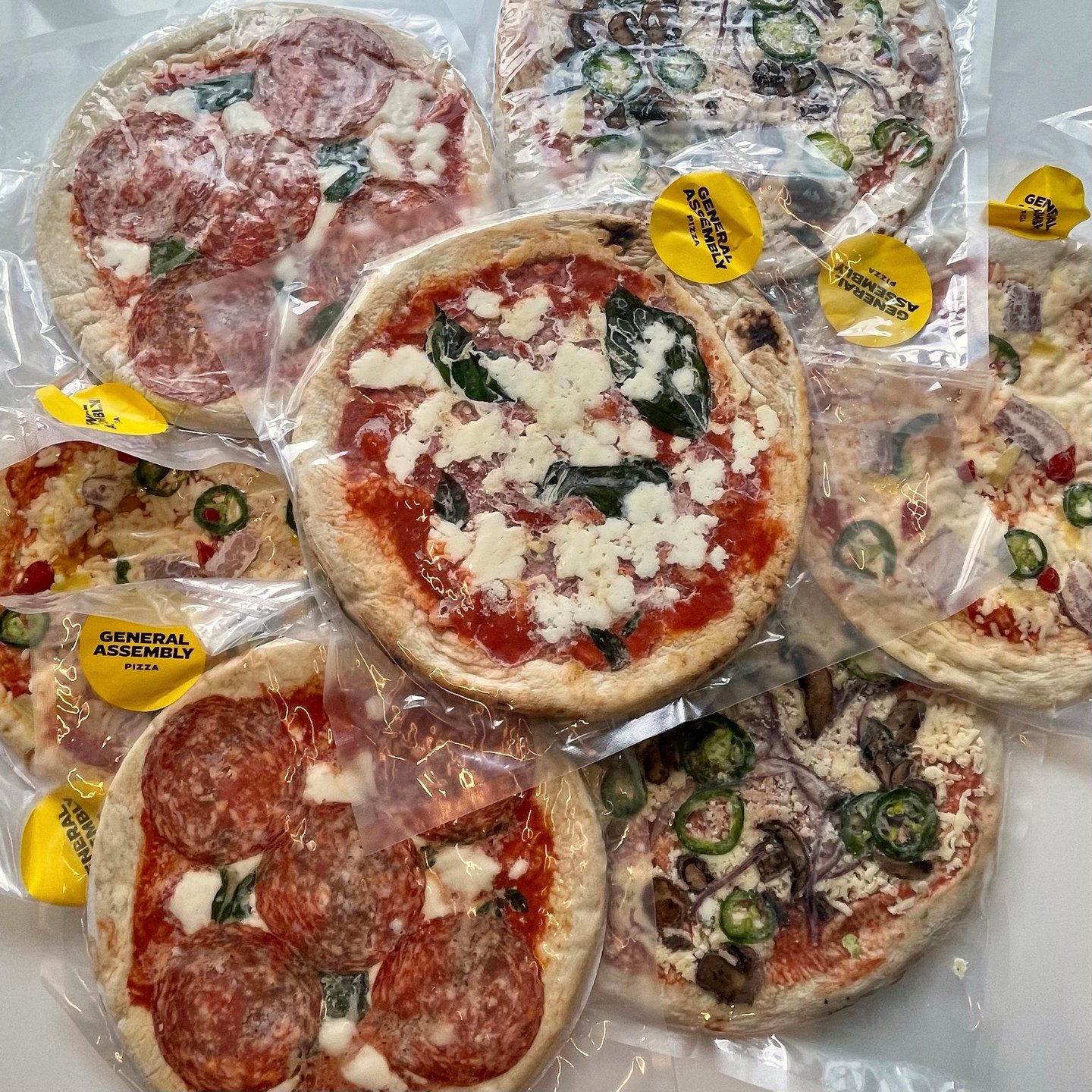 A stack of wrapped par-frozen pizzas from General Assembly