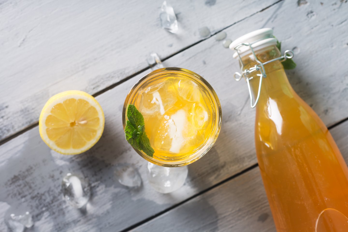 Kombucha is a drink produced by fermenting tea with symbiotic culture of bacteria and yeast. A bottle of lemon kombucha next to a full glass of the healthy drink and a slice of lemon