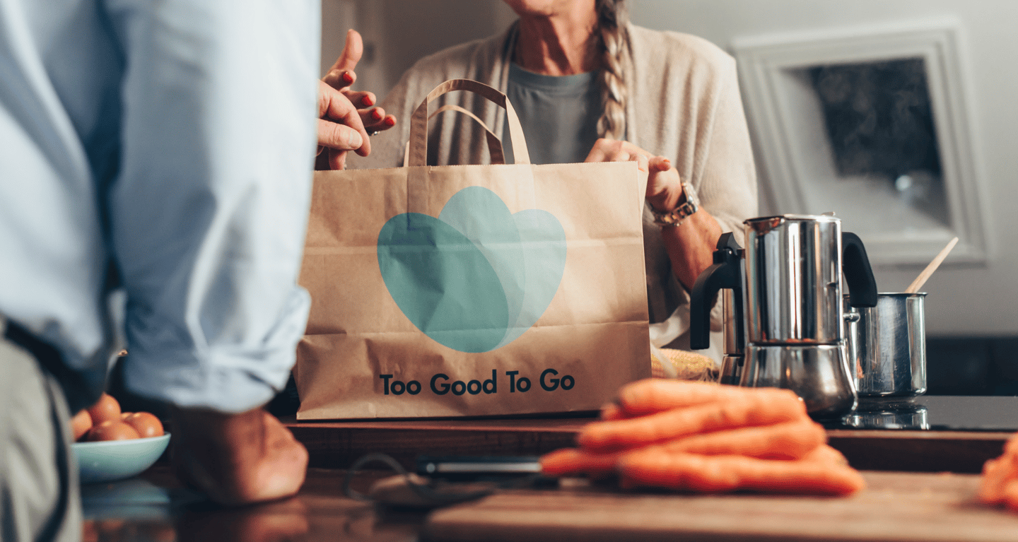 A man and woman standing in a kitchen unpacking a Too Good To Go paper bag