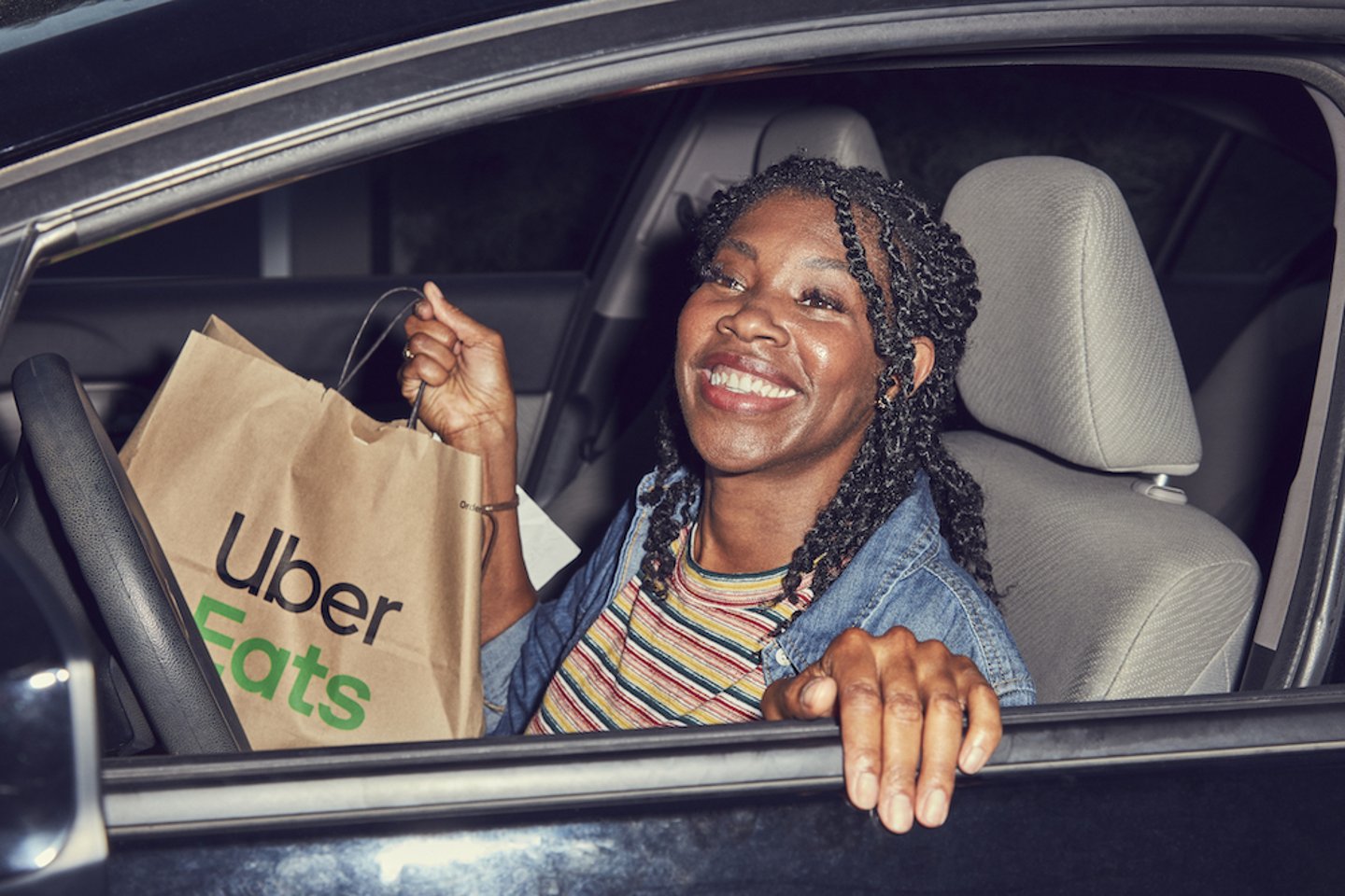 Female Uber driver holding an Uber Eats bag as she gets out of her car