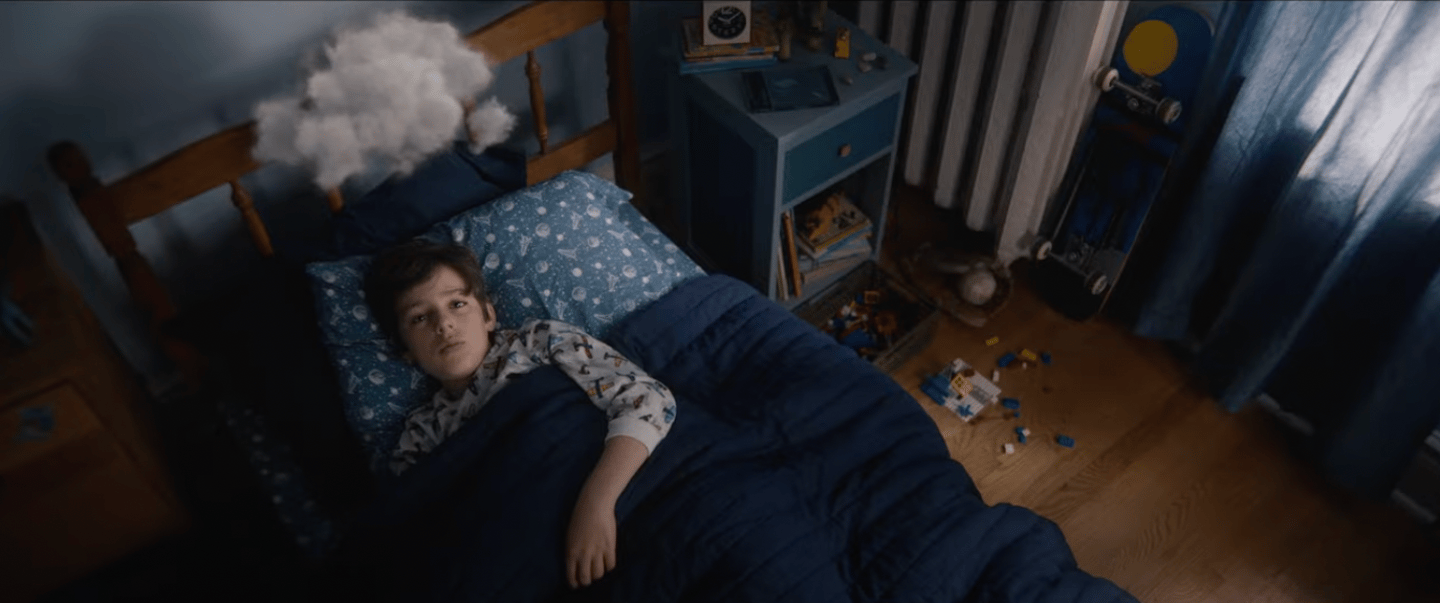 Young boy lying in bed with a cloud over his head