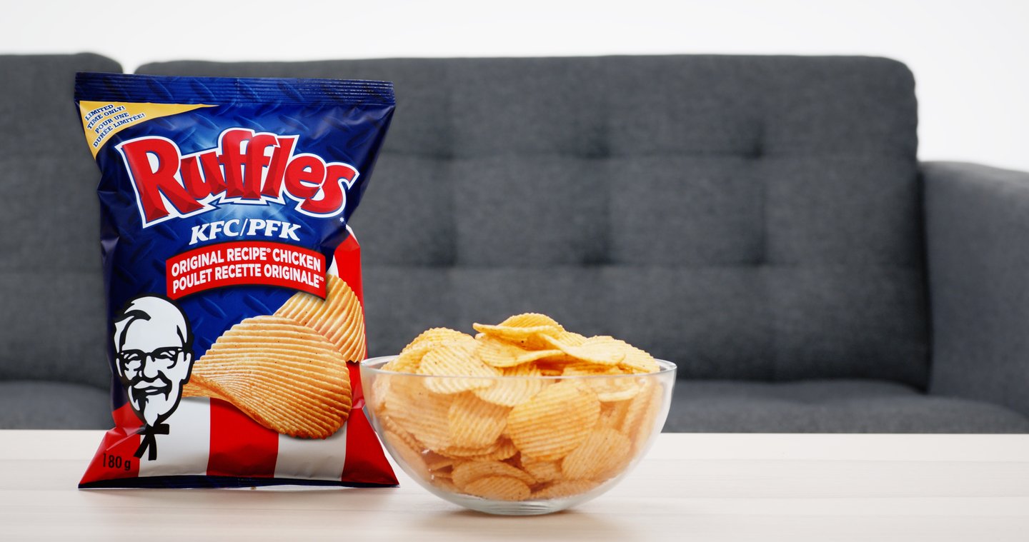 a bag of Ruffle chips beside a bowl of chips on a coffee table next 