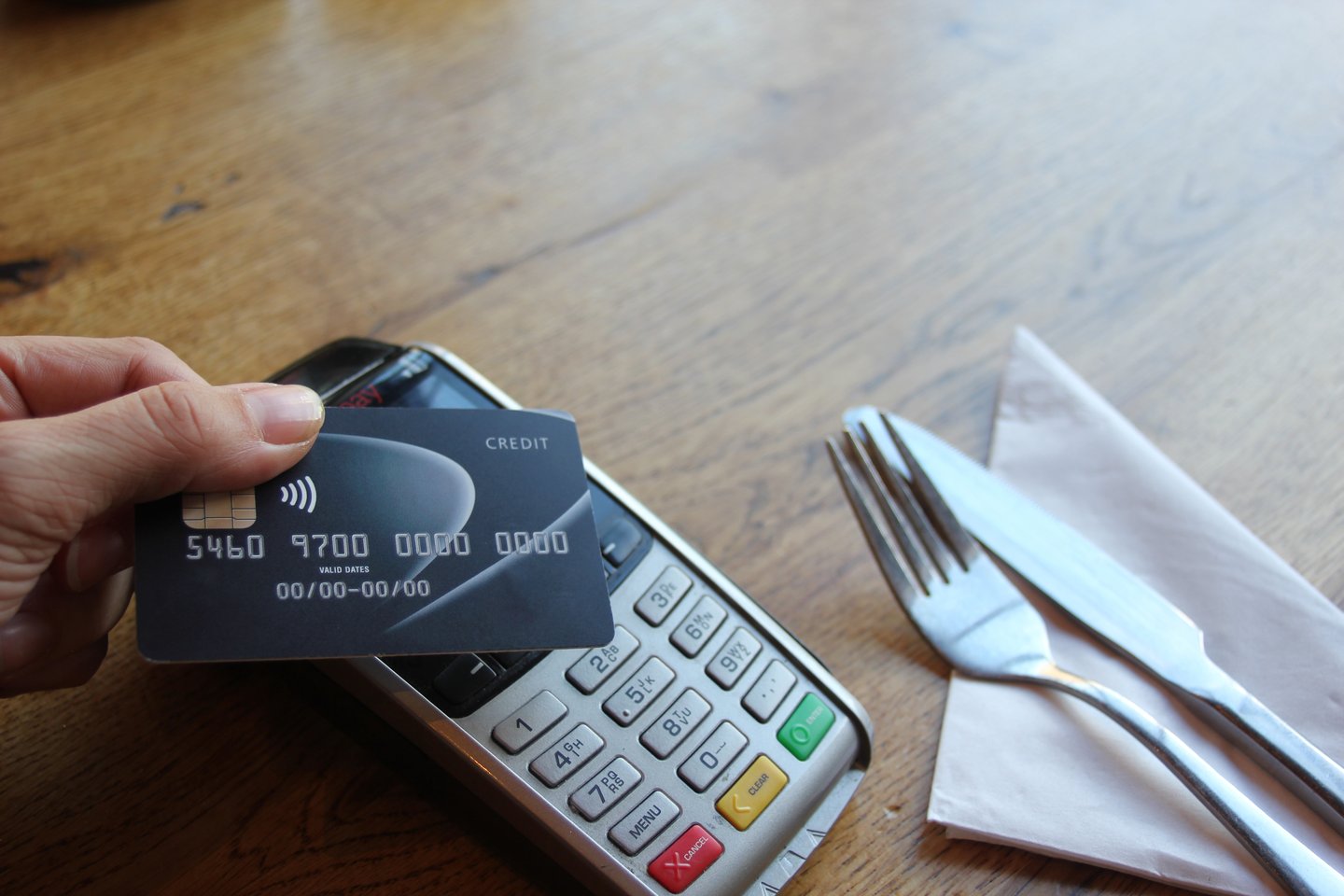 A hand holding a debit card and tapping in on the payment terminal
