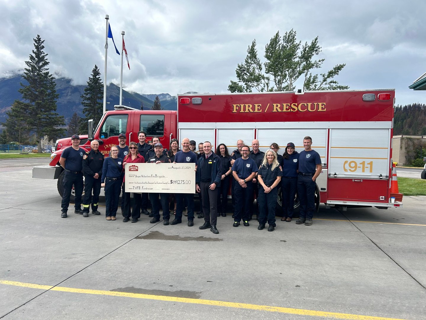 Firefighters holding a large cheque standing in front of a fire truck