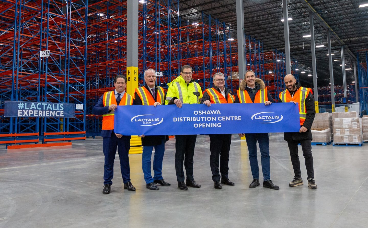 A group of people standing in a warehouse holding a large ribbon ready to be cut 