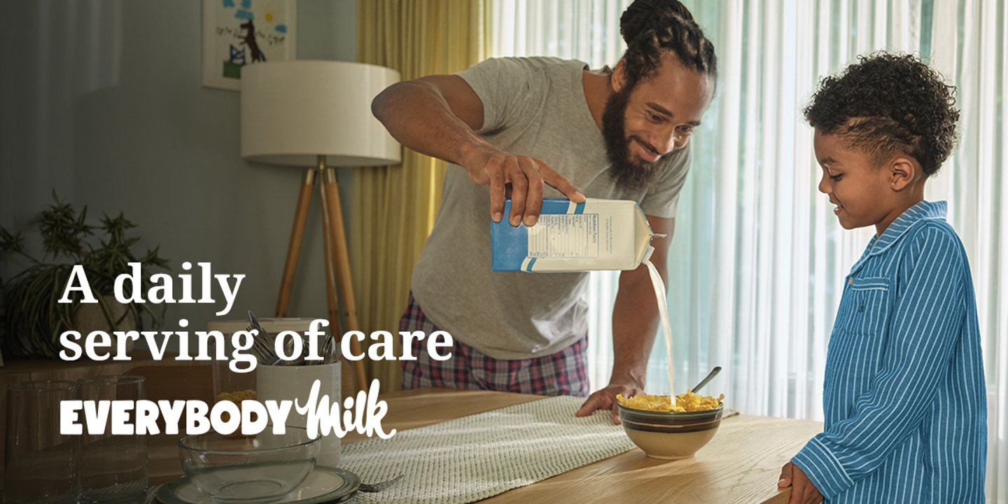 A father pouring milk into a cereal bowl while his young son watches