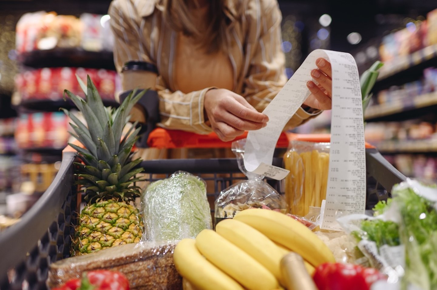 Woman looks at a grocery bill above a shopping cart of produce