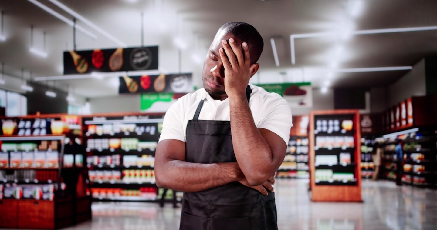 Employee stands in a grocery store with his hand on his face