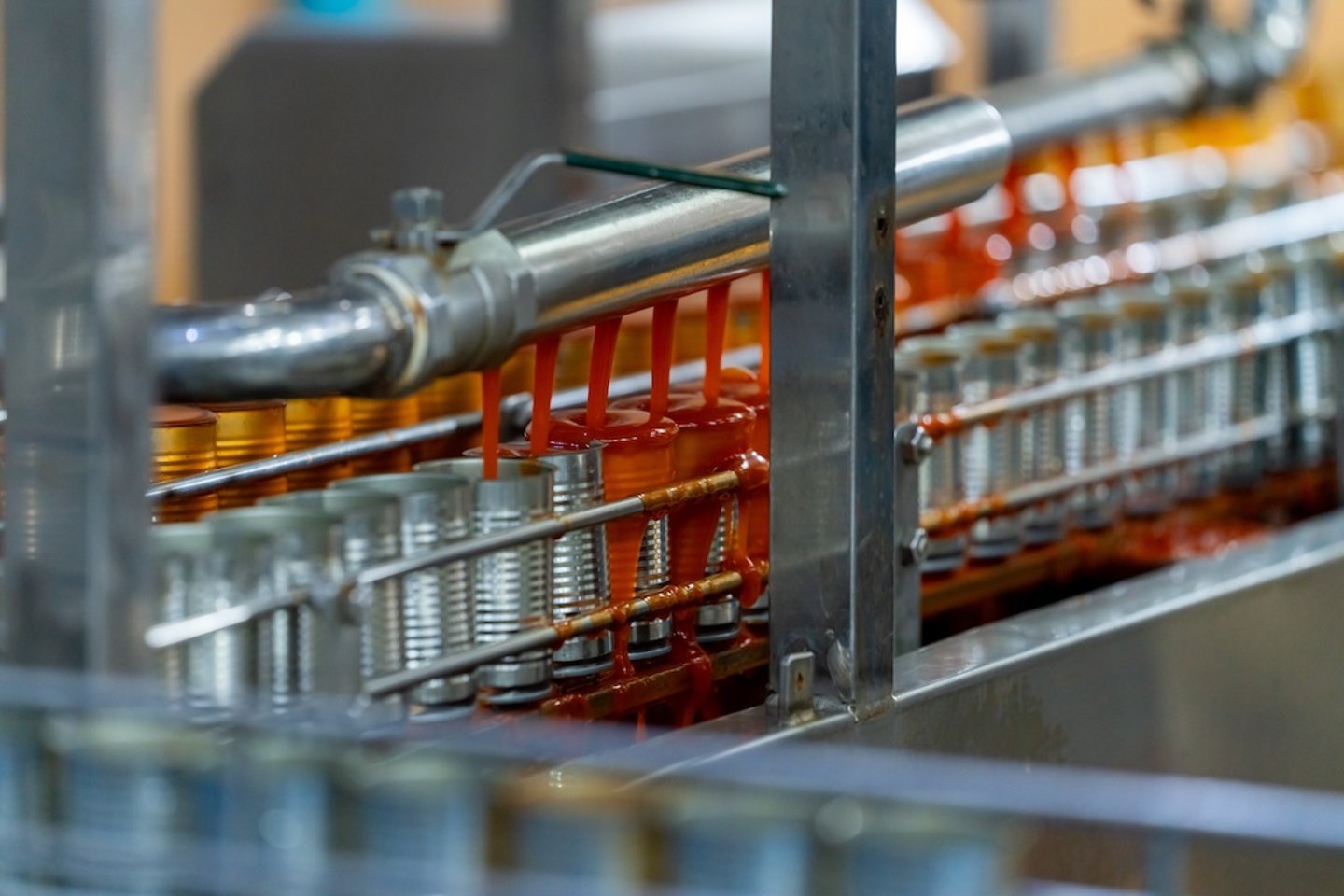 Cans on a manufacturing line getting filled with a red sauce.