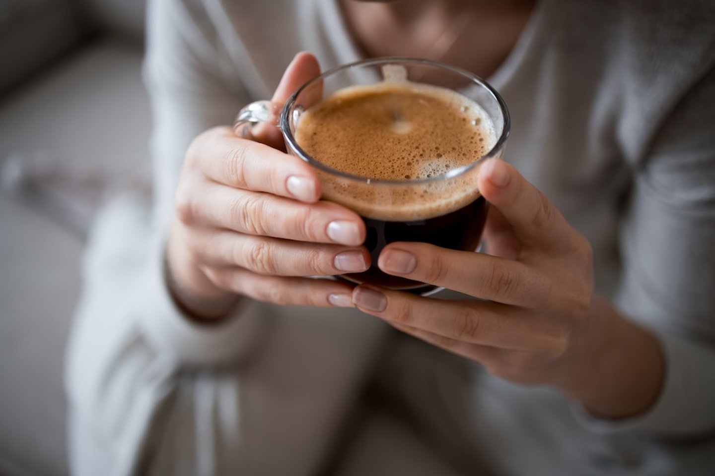 Two hands holding a cup of black coffee in a clear mug