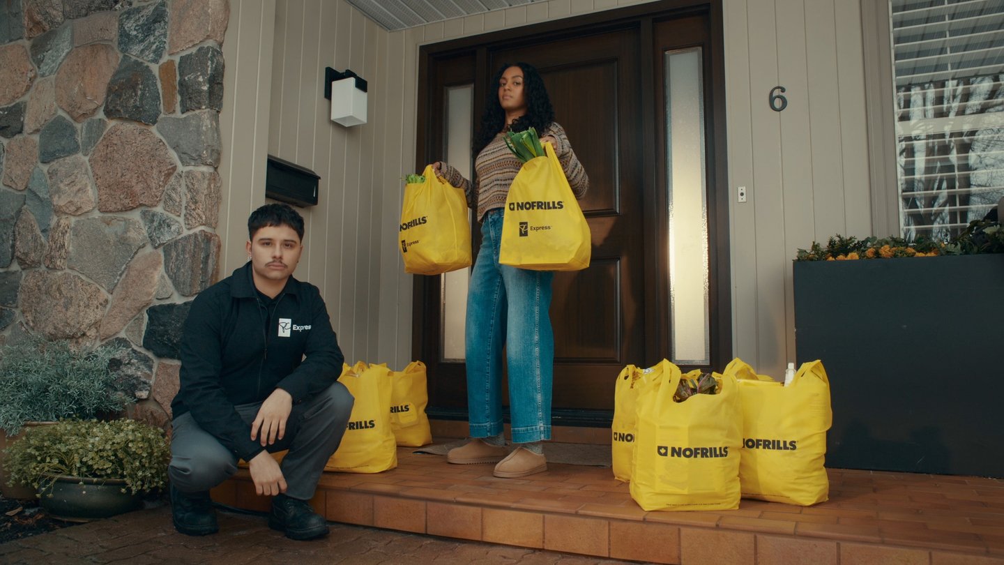 A woman standing on her porch holding No Frills bags