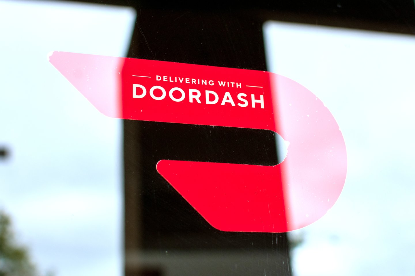 Close up. A red sticker decal on a restaurant door advertising delivery service available through DoorDash on-demand prepared food delivery service