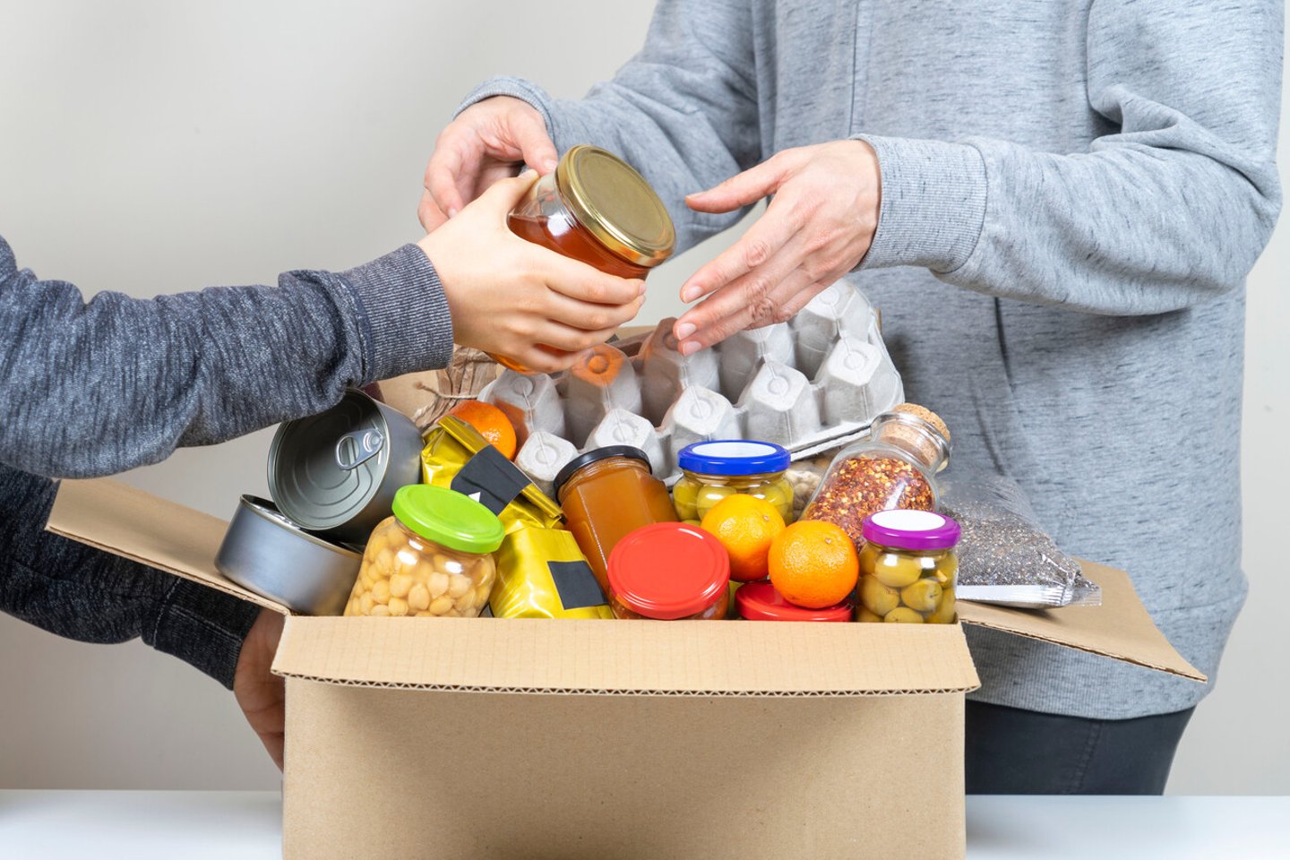 Volunteers hands putting grocery products, foodstuff to food donations box; Shutterstock ID 1868920810