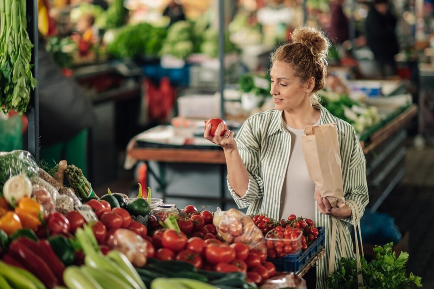 Portrait of female customer standing near market stall with paper bag in hands and shopping fresh organic tomato at farmer's market. Young shopper woman purchasing fresh products at food market.; Shutterstock ID 2455755411