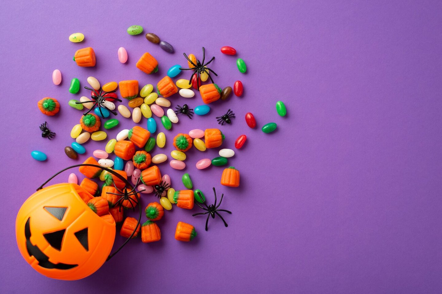 Top view photo of halloween decorations pumpkin basket with candies and spiders on isolated violet background; Shutterstock ID 2191379013