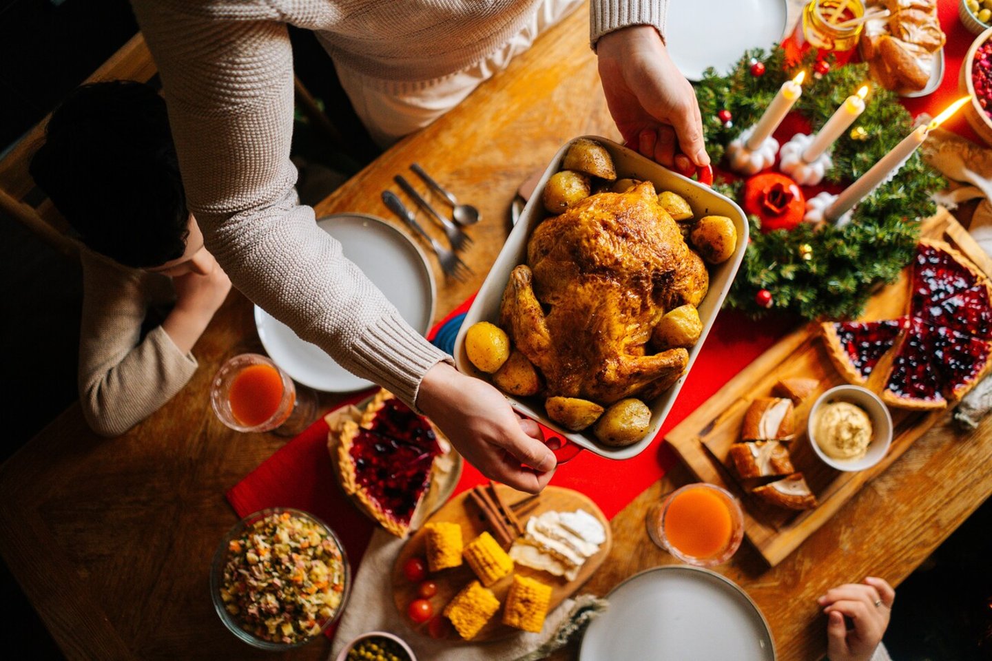 Close-up top view of young father male putting dish with baked hot turkey on holiday dinner table served for Christmas family party, celebrating thanksgiving day with roasted turkey for dinner.; Shutterstock ID 2226983789