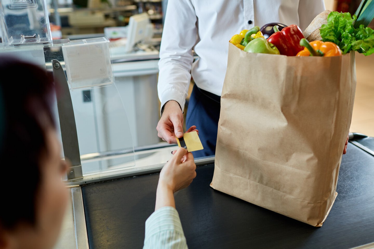 The man's hand  buyer pays by card for purchase in paper bag with healthy fresh meal near  cashier at the supermarket during shopping; Shutterstock ID 683756188