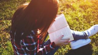 Relaxed young woman reading a book at the lawn with sun shining