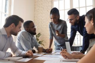 Serious multiracial corporate business team and black leader talk during group briefing, focused diverse colleagues brainstorm discuss report paperwork engaged in teamwork at meeting gather at table