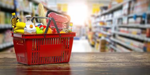 A shopping basket full of food sits on a table at the end of a grocery aisle