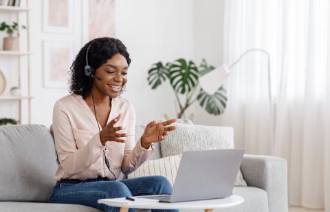 Video Conference. Smiling african woman having web call on laptop at home, talking at camera while sitting on sofa in living room