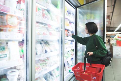 A girl with a basket takes frozen foods from the supermarket's refrigerator. The girl chooses goods in the store. Shopping in the supermarket.
