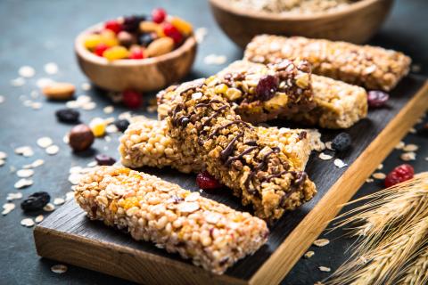 Granola bar with nuts, fruit and berries on cutting board at dark stone table.