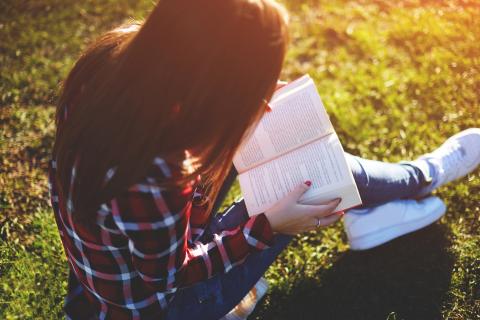 Relaxed young woman reading a book at the lawn with sun shining