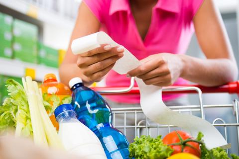 Woman checking a long grocery receipt leaning to a full shopping cart at store.