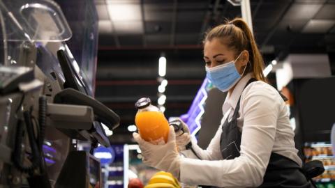 Working during corona virus pandemic. Cashier in grocery store wearing mask and gloves fully protected against the virus.