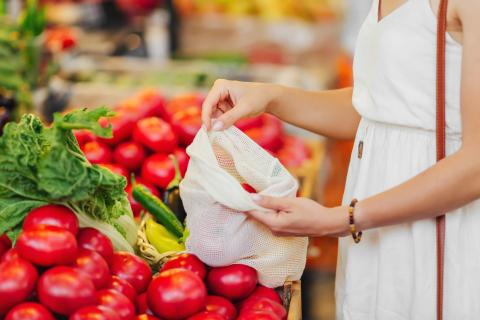Female hands puts fruits and vegetables in cotton produce bag at food market.
