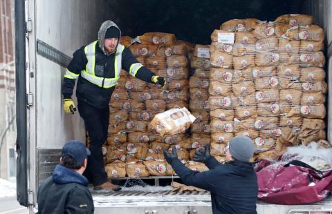 A man standing in the back of a truck passing out bags of potatoes