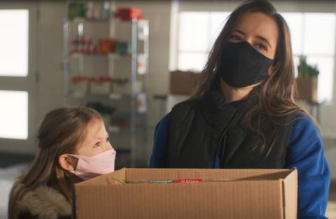 Mother and daughter wearing masks and holding a cardboard box full of food