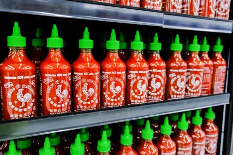 Plastic bottles of Huy Fong Food Sriracha hot chili sauce in a supermarket aisle