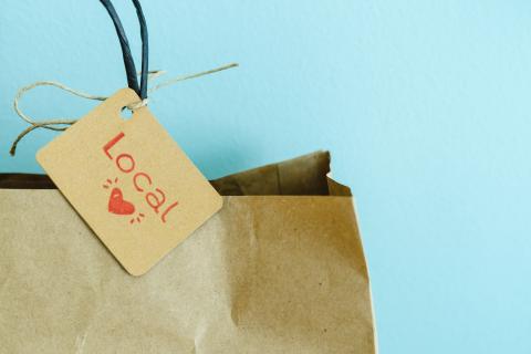 Paper shopping bag with label on blue background. Label with heart and text LOCAL. Shopping concept