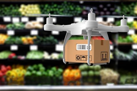 Drone holding a cardboard box hovering in a produce department