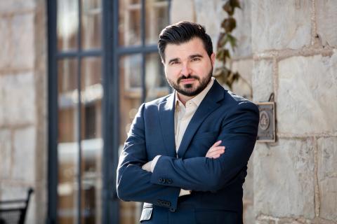 A man standing, arms folded in front of a brick wall