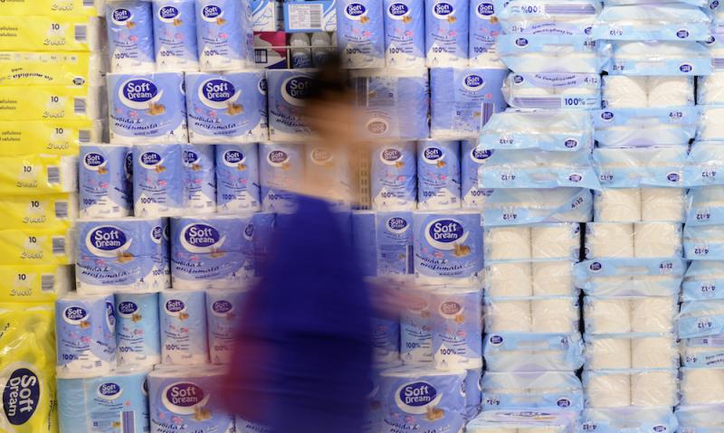 A grocery shoppers walks by a display of toilet paper
