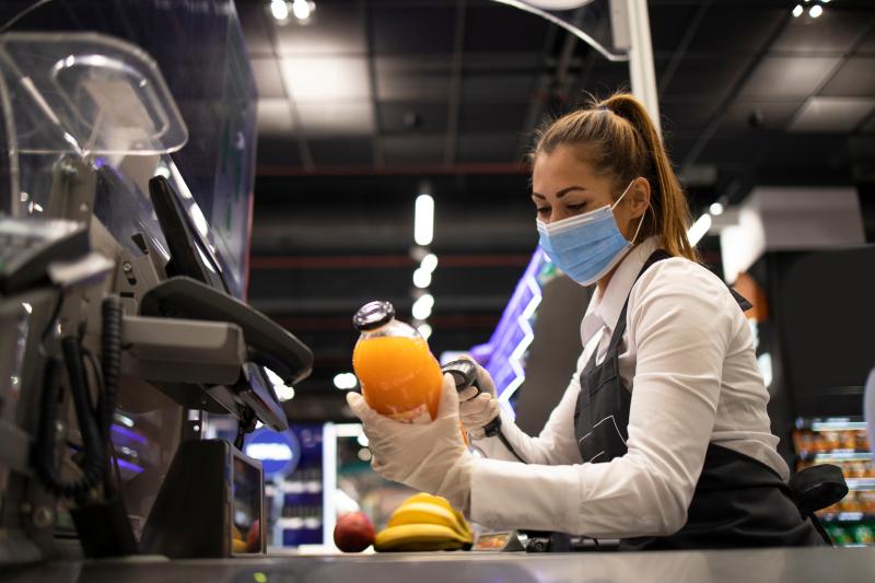 Working during corona virus pandemic. Cashier in grocery store wearing mask and gloves fully protected against the virus.