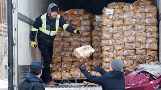 A man standing in the back of a truck passing out bags of potatoes