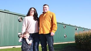 A husband, wife and child standing in front of a barn